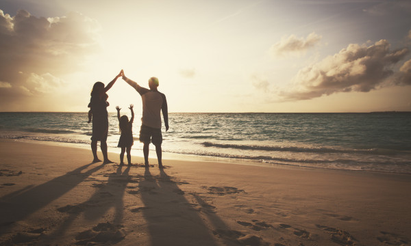 three people stand on a beach next to an ocean in shadow holding their arms above their heads