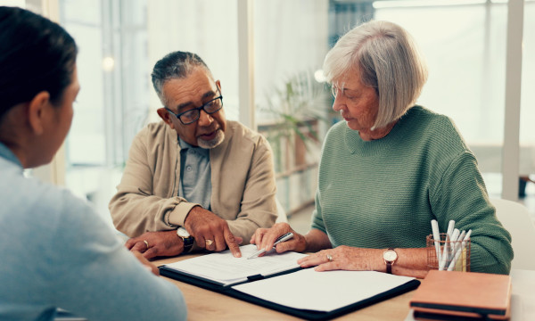 an older man and woman sit at a table review documents with another man