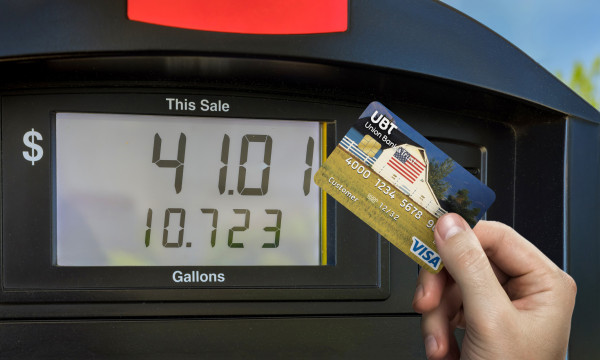 a person holds their ubt debit card up next to a gas pump