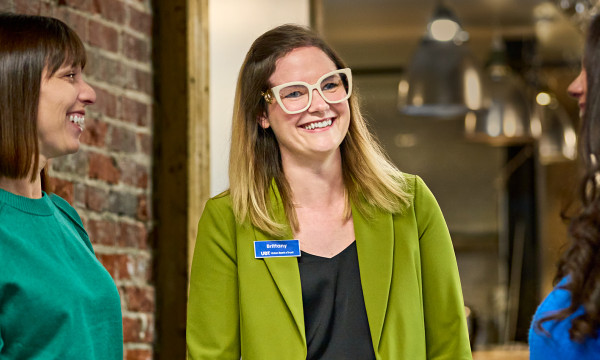 Brittany Planos, UBT's Financial Literacy Program Manager, wearing a green blazer and white glasses