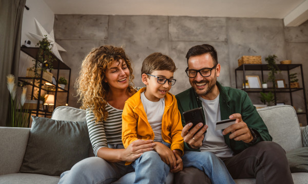 a mom and dad sit with their son on a couch looking at a phone and debit card