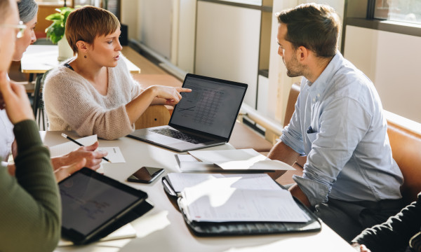 Colleagues sit around a desk looking at a laptop screen