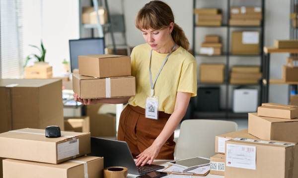 a woman stands holding a box in a room full of boxes